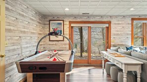 A room with a pool table, a sofa, and a door leading to a view of trees.