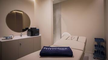 A modern hotel room with a bed, a bedside table with a coffee machine, a mirror, and a blue trolley.