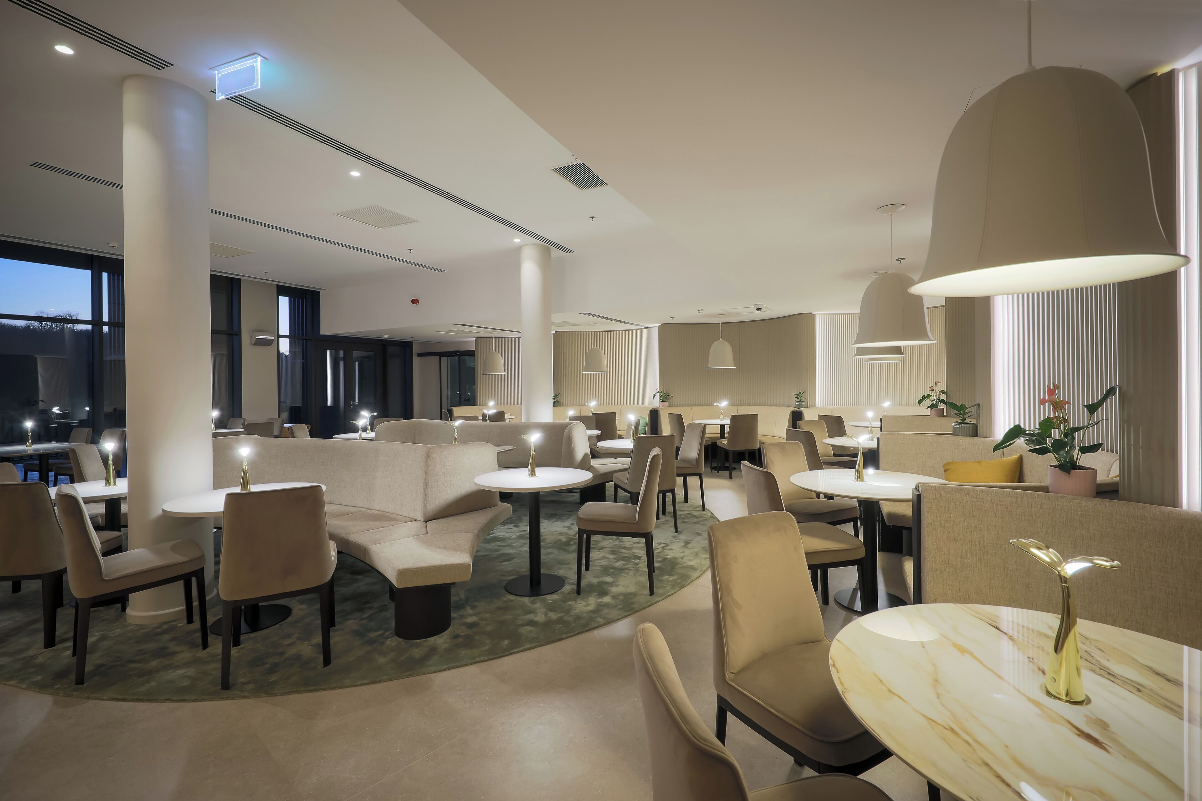 A modern hotel lobby with seating areas, tables, and large pendant lights.