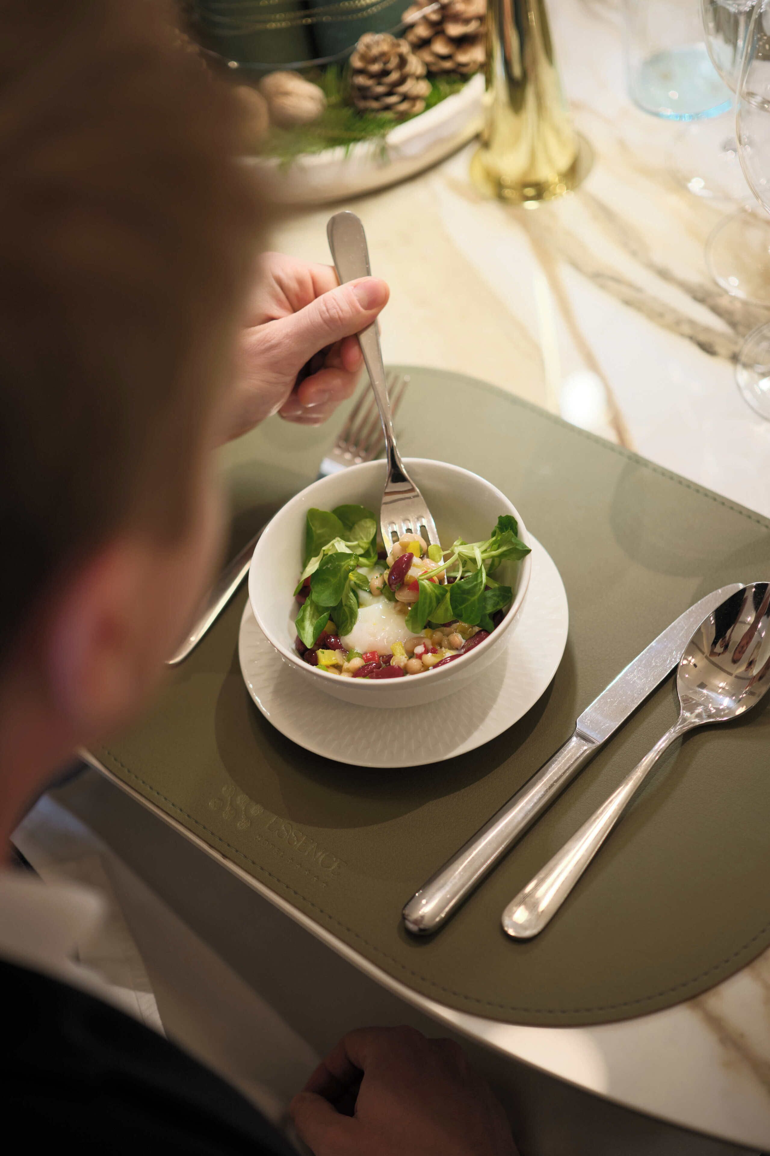 Una mesa de comedor con un tazón de ensalada, un tenedor y un cuchillo.