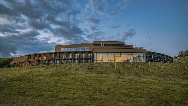 A modern building with a curved facade, large windows, and a flat roof. - Hotel Essence (Pogány)