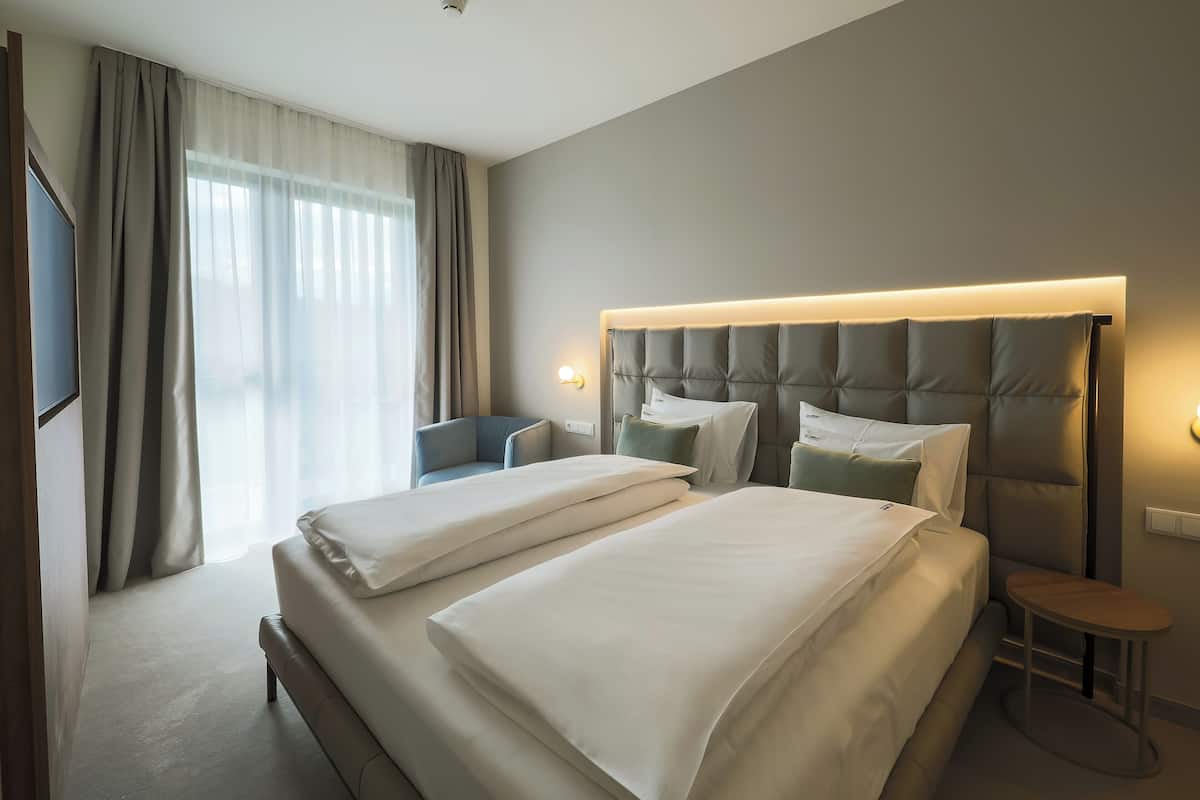 Quarto de hotel com duas camas, uma cadeira, uma mesinha e uma televisão.