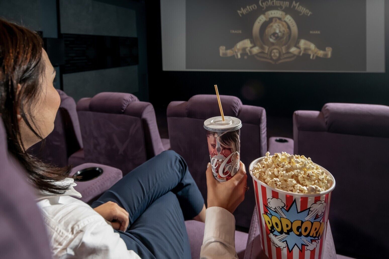 Iemand zit in een bioscoopzaal voor een groot scherm waarop een filmtitel staat.