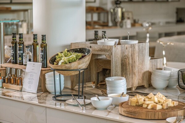 A buffet setup with various food items, including a bowl of salad, cheese, and multiple bottles of beverages. - Hotel Essence (Pogány)
