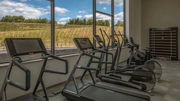 Ein Fitnessstudio mit mehreren Laufbändern und Trainingsgeräten, große Fenster mit Blick auf eine Wiese.