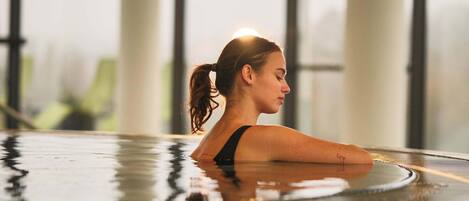 A person in a hot tub in a modern indoor setting with large windows.