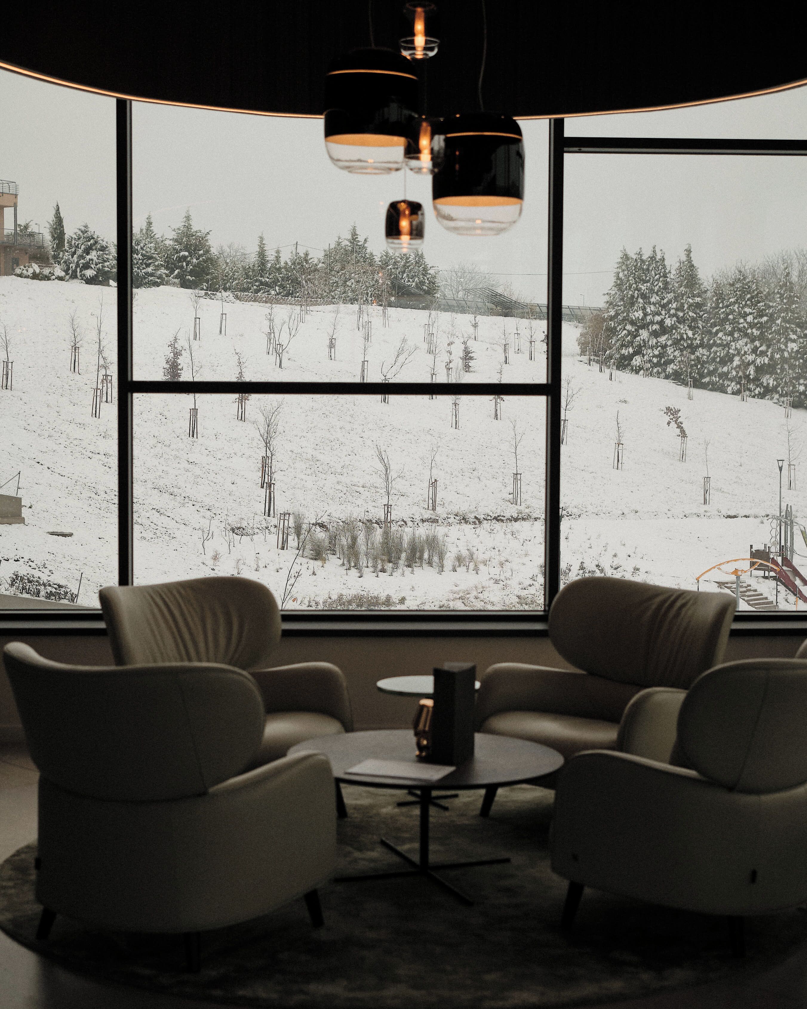 A modern room with large windows, two armchairs, a small table, and hanging pendant lights.