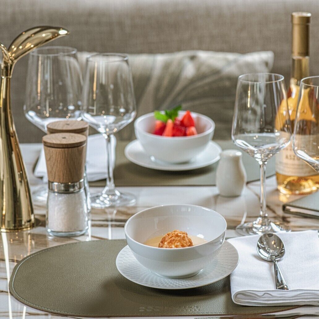 A dining table set with a bowl of dessert, wine glasses, and a bottle of wine.