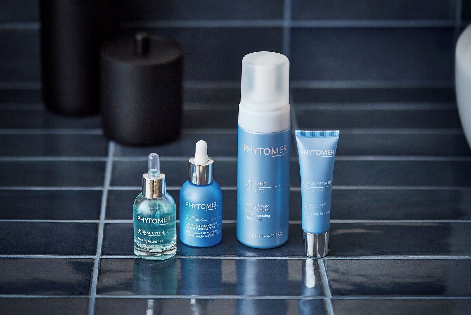A bathroom with four skincare products from Phytomer on a tiled floor.