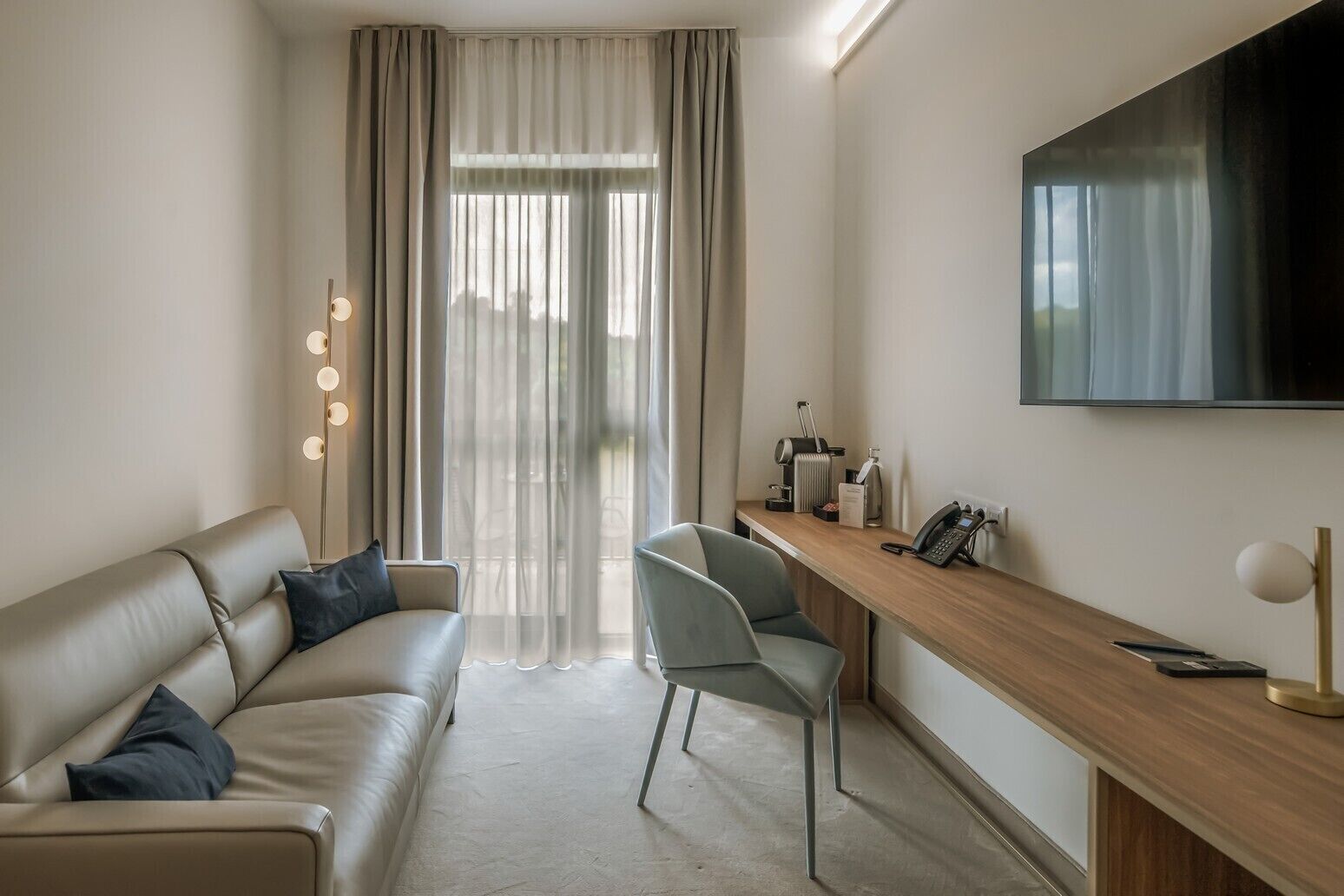 Een moderne hotelkamer met een leren bank, een bureau met telefoon en een grote televisie aan de muur.