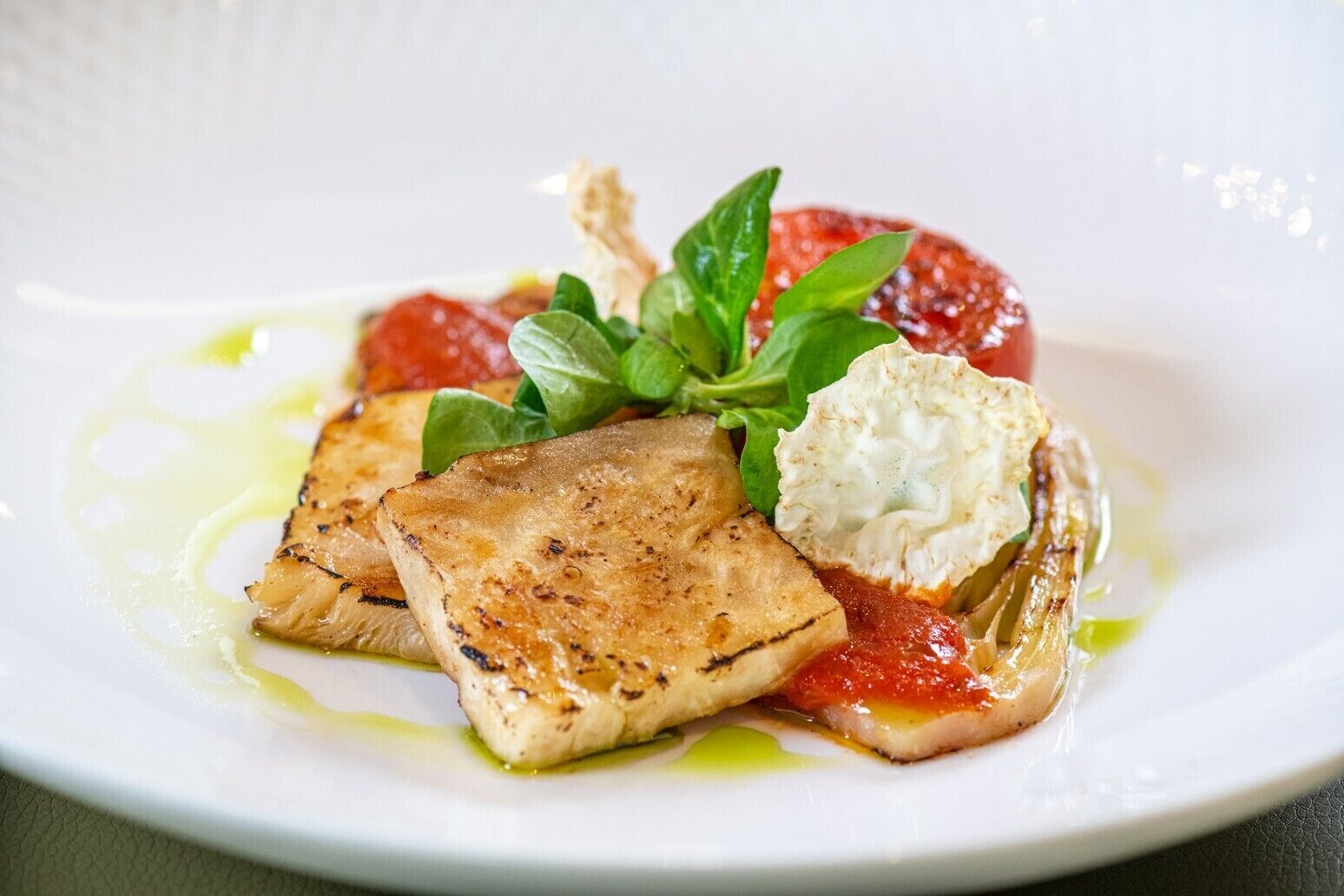A plate with grilled fish, a dollop of cream, and a slice of tomato.