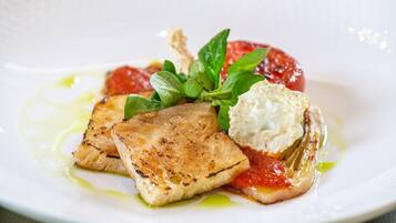 A plate with grilled fish, a dollop of cream, and a slice of tomato.