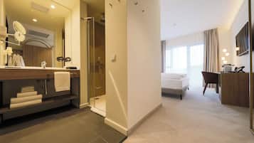 Een moderne hotelbadkamer met douche, een wastafel met spiegel en een handdoekrek.