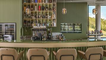 A bar area with a green-striped wall, shelves of liquor bottles, a coffee machine, and bar stools.