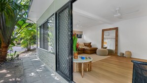 A modern living room with a wooden floor, a brown leather sofa, a round wooden coffee table, and a large mirror. - Belle Escapes Sun Rose in Palm Cove (Palm Cove)