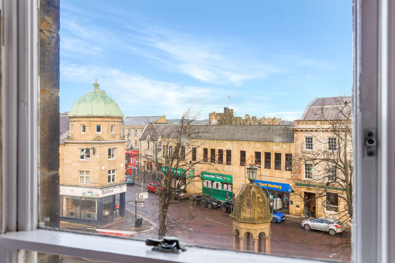 Une vue d’une rue bordée de bâtiments historiques, avec notamment un tramway vert et un bâtiment portant l’inscription « Bailey’s ».
