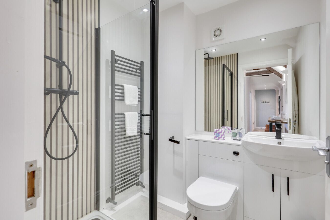 Een moderne badkamer met een douchecabine van glas, een wit toilet en een wastafel met spiegel.