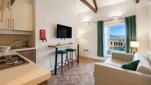 A compact living space with a kitchenette, a dining area with stools, a sofa, and a TV mounted on the wall. - Apartment with castle view (Alnwick)