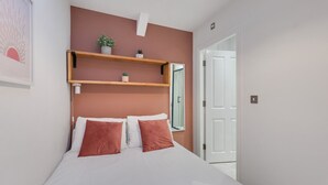 A bedroom with a bed, two pillows, a nightstand, a wall-mounted shelf with plants, and a door to another room. - Apartment with castle view (Alnwick)