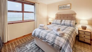 A neatly arranged bedroom with a bed, two bedside tables, a window with curtains, a headboard, and a wall-mounted picture.