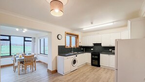 A modern kitchen with white cabinets, a washing machine, and a dining area with a table and chairs.