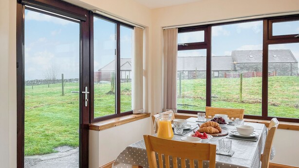 A dining area with a table set for breakfast, including croissants, fruit, and a jug of orange juice.