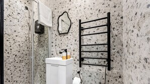 A bathroom with a shower, a sink with toiletries, a towel rack, and a toilet.