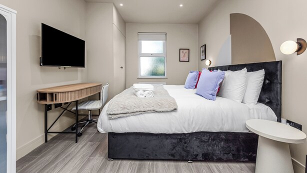 A bedroom with a bed, a desk, a TV, and a window.