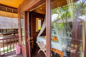 A wooden room with a bed, a window, and a balcony with a chair. - Nanuk's Bungalows (Bali)