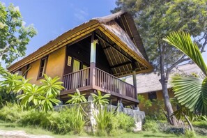 A traditional thatched-roof house with a balcony, surrounded by lush greenery. - Nanuk's Bungalows (Bali)