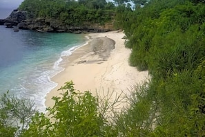 A beach with clear water, sandy shore, and surrounding greenery. - Nanuk's Bungalows (Bali)