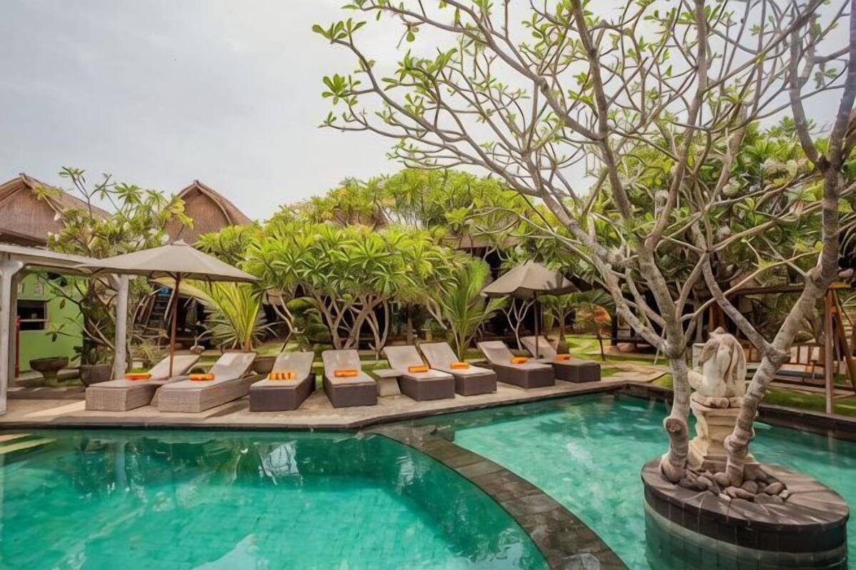 A pool area with lounge chairs, a small pavilion, and tropical plants.
