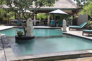 A swimming pool with lounge chairs and a thatched-roof structure in the background. - Nanuk's Bungalows (Bali)