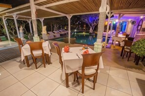 An outdoor dining area with tables and chairs, a pool, and a covered walkway. - Nanuk's Bungalows (Bali)