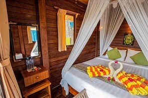 A wooden cabin room with a bed, a nightstand, a mirror, and a window with curtains. - Nanuk's Bungalows (Bali)