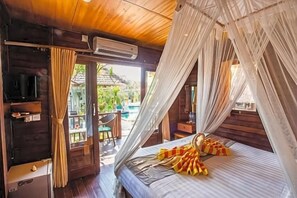A room with a bed, a television, and a balcony with a table and chairs. - Nanuk's Bungalows (Bali)