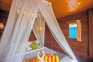A room with a canopy bed, a small window with curtains, and a nightstand with a decorative item. - Nanuk's Bungalows (Bali)