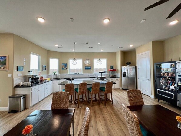 Una cocina moderna con una isla central, zona de comedor con sillas de mimbre y una máquina expendedora.