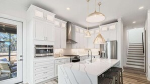 A modern kitchen with white cabinetry, a large island with bar stools, stainless steel appliances, and pendant lighting. - Luxury Home | Golf Cart | Wavecrest Retreat | Pool | Inlet Beach (Inlet Beach)
