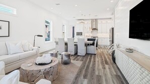 A modern living room with a stone coffee table, white sofa, and a dining area with chairs. - Luxury Home | Golf Cart | Wavecrest Retreat | Pool | Inlet Beach (Inlet Beach)