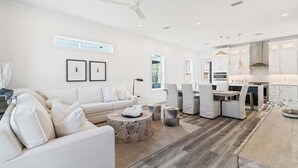 A modern living room with a sofa, coffee table, and dining area. - Luxury Home | Golf Cart | Wavecrest Retreat | Pool | Inlet Beach (Inlet Beach)