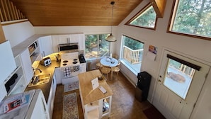 Une cuisine compacte équipée d’une cuisinière, d’un four à micro-ondes et d’un évier, un coin repas avec une table et des chaises, et de grandes fenêtres offrant une vue sur l’extérieur.