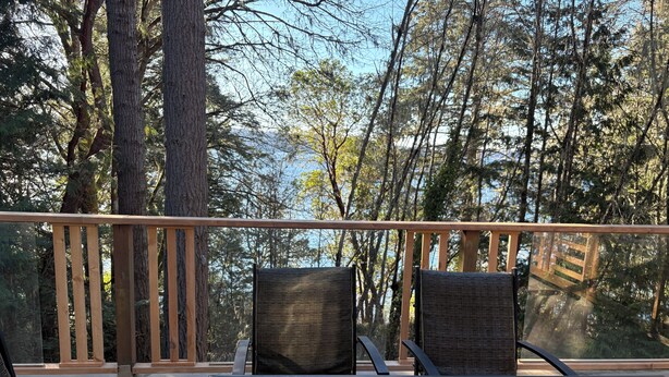 Un balcon avec une table en verre et deux fauteuils en osier, donnant sur une zone boisée.