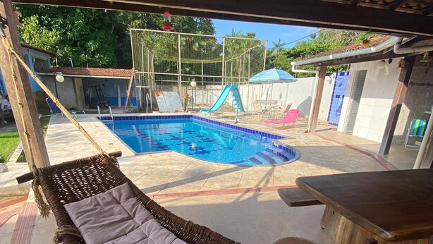 A hammock under a wooden pergola by a swimming pool with a slide.