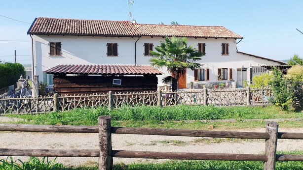Un bâtiment à deux étages, avec un toit recouvert de tuiles, une clôture en bois à l’avant et un palmier sur la droite.