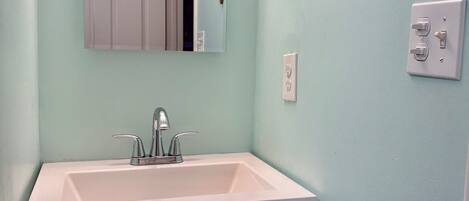 A bathroom with a white sink, a mirror, and a wall-mounted light switch.