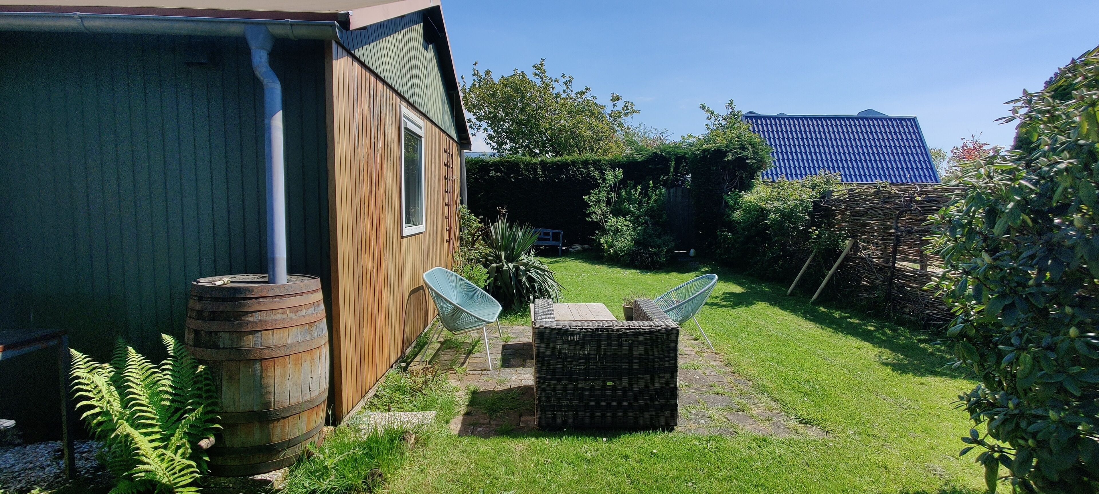 Ein Holzhaus mit Fenster, Fass, Stuhl und einem kleinen Garten.