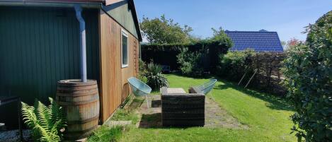 Ein Holzhaus mit Fenster, Fass, Stuhl und einem kleinen Garten.