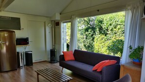 Una sala de estar con un sofá, una silla, una mesa de centro de madera, un refrigerador, un microondas, un bote de basura y un calentador.