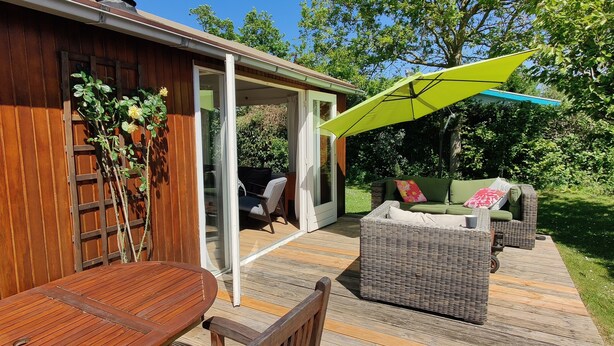Una terraza de madera con una mesa, sillas y un sofá de mimbre, además de un paraguas verde.